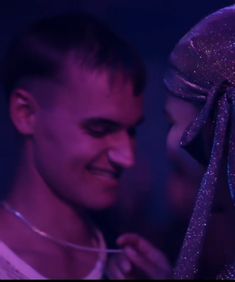 a man and woman standing next to each other in front of a blue background with purple lights