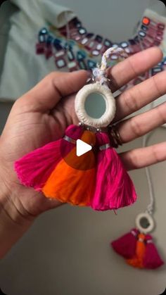 a hand holding a small keychain with tassels and beads on it