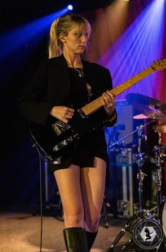 a woman in short shorts and boots playing an electric guitar on stage with blue lights behind her