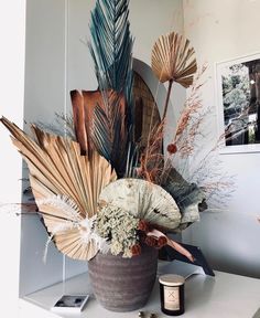 an arrangement of flowers and leaves in a vase on top of a white countertop