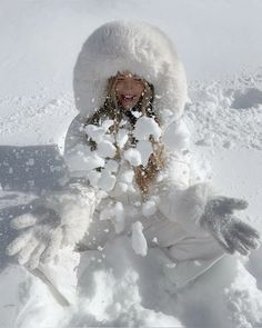 a woman is playing in the snow with her hands and feet covered by snowballs