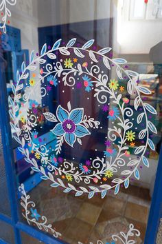 a decorative glass window with flowers and leaves painted on the glass, in front of a blue door