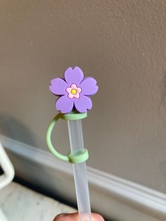 a hand holding a plastic flower on top of a toothbrush holder in front of a wall