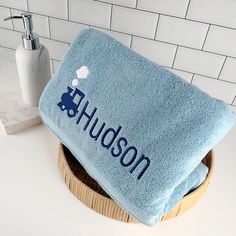 a blue towel that says hudson on it is sitting in a wooden basket next to a white tile wall