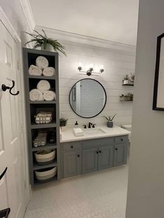 a bathroom with gray cabinets and white towels on the shelves, along with a large round mirror