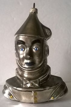 a silver statue with a helmet on it's head and blue eyes, sitting in front of a white wall