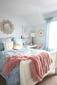 a white bed topped with a pink fluffy blanket next to a window covered in blue curtains