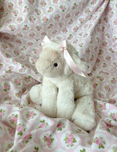 a white stuffed animal sitting on top of a pink bed sheet covered in floral sheets