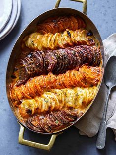 a pan filled with cooked potatoes on top of a blue tablecloth next to silverware