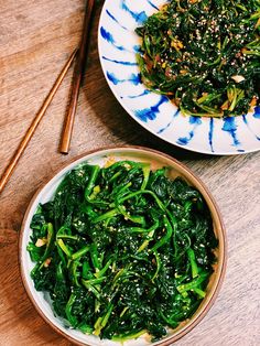 two bowls filled with greens and chopsticks on a table next to each other