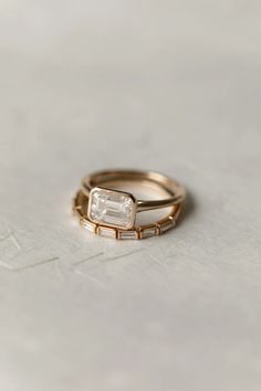 two gold wedding bands with an emerald stone in the middle, on top of a white surface