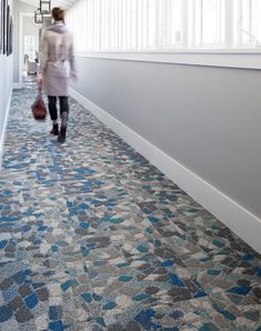 a woman walking down a long hallway with blue and gray carpeting on the floor