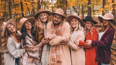 a group of women standing next to each other in front of a wooden fence and trees