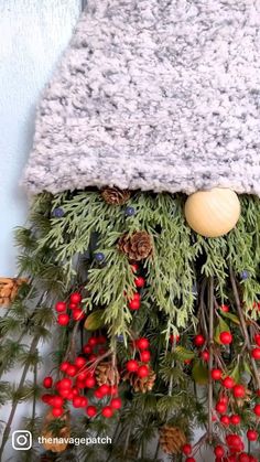 a knitted hat hanging from the side of a tree with berries and pine cones