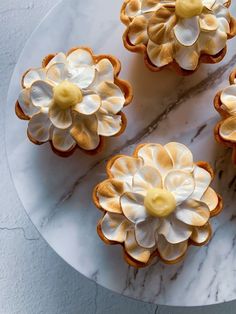 four cupcakes with white and yellow frosting flowers on a marble platter