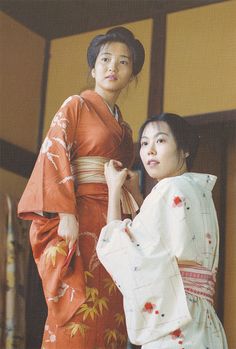 two women dressed in traditional japanese clothing standing next to each other and looking at the camera