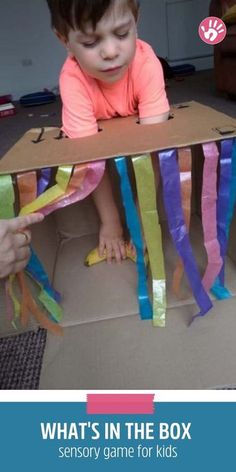 a young child is playing in a box that has ribbons on it and the words, what's in the box?