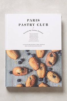 the book paris pastry club is sitting on top of a wooden table with blueberries and almonds