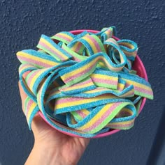 a hand holding a pink bowl filled with multicolored hair ties on top of a blue wall