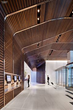 two people are walking down the hallway in an office building with wood slats on the ceiling