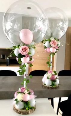 two clear balloons with flowers and greenery on them sitting on a table in the middle of a room