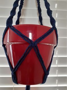 a red bucket hanging from the side of a window with blue string attached to it