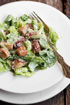 a white plate topped with lettuce and croutons next to a fork