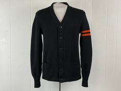 "Vintage 1940s letterman school cardigan sweater. Made of black knit wool with orange stripes on left arm. Has a six button front and two pockets. Has owner's name ART KRELLWITZ embroidered on patch inside. Made by NELSON KNITTED MILLS DULUTH, MINN. About a size small. Actual measurements are:   39\" around the chest   37\" around the waist   18.5\" shoulder seam to shoulder seam   27\" shoulder seam to end of cuff, uncuffed  27\" overall length   4\" banded cuffs In very good condition." Black Retro Cotton Cardigan, Vintage Black Fitted Sweater, Vintage Workwear Sweater With Button Closure, Vintage Sweater With Button Closure For Work, Vintage Black Cardigan With Button Closure, Vintage Wool Sweater For Workwear, Vintage Black Sweater With Buttons, Black Vintage Cardigan For Fall, 1940s Sweater