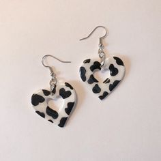 a pair of heart shaped earrings with black and white spotted cow print, hanging from silver earwires