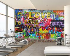 a gym room with colorful graffiti on the wall and exercise equipment in front of it