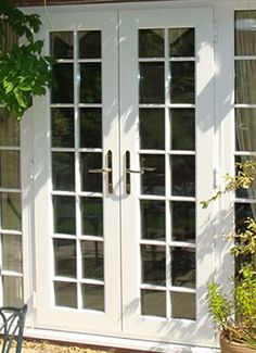 a white double door sitting next to a wooden bench in front of a house with glass doors