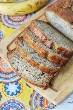 sliced loaf of banana bread on a cutting board next to two bunches of bananas