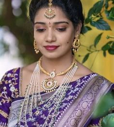 a woman in a purple and gold sari with pearls on her neck, necklaces and