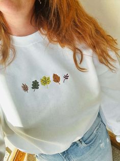 Introducing our Autumn Leaves Embroidered Sweatshirt, the perfect addition to your fall wardrobe. This 2D Crewneck Sweatshirt is not only stylish but also a thoughtful gift for your loved ones. With its exquisite embroidery and cozy design, it effortlessly combines fashion and comfort. Our sweatshirt features a stunning autumn leaves design meticulously embroidered on the front, showcasing the beauty of nature in its vibrant colors. The intricate detailing and precise stitching make this sweatsh Cozy Sweatshirt Aesthetic, Embroidery Ideas Machine, Fall Embroidery Designs Sweatshirt, Cute Fall Sweatshirts, Embroidered Gifts Ideas, Embroidery Sweatshirt Ideas, Hand Embroidery Sweatshirt, Fall Leaves Embroidery, Hand Embroidered Sweatshirt