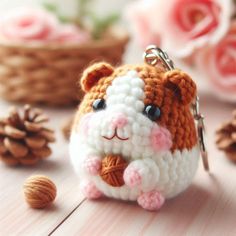 a small crocheted hamster keychain sitting next to some pine cones