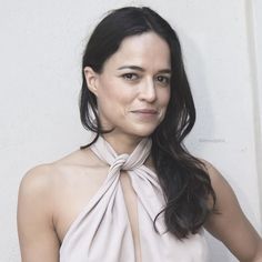 a woman with long hair wearing a halter top and posing for the camera in front of a white wall