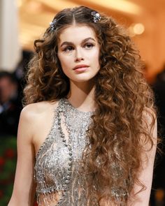 a woman with long, curly hair wearing a silver dress at the mete awards