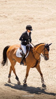 a woman riding on the back of a brown horse across a sandy field with no grass