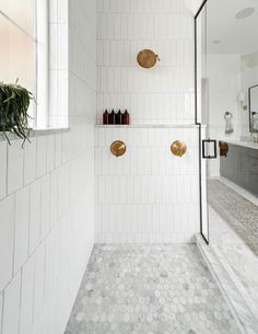 a white tiled bathroom with gold accents and mirrors on the wall, along with a walk in shower