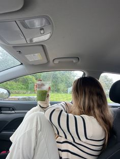 a woman sitting in the back seat of a car holding up a green drink with her hand