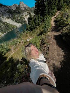 a woman taking a selfie in the mountains with trees and water behind her on a sunny day