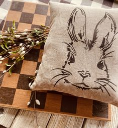 a pillow with a rabbit drawn on it sitting next to some dried flowers and twigs