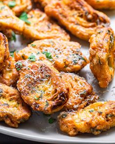 some fried food on a white plate with parmesan cheese and green garnish