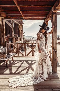 a woman in a cowboy hat standing on a wooden deck wearing a white lace dress