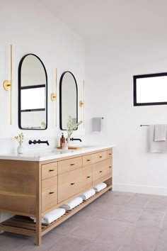 two mirrors on the wall above double sinks in a bathroom with wood cabinets and white walls