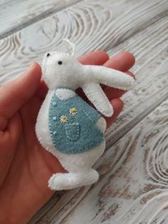 a hand holding a white stuffed animal with daisies on it's chest and the back of its body