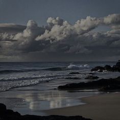 the sky is filled with white clouds over the water and rocks on the beach near the ocean