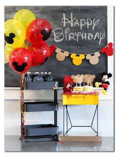 a birthday party with balloons and mickey mouse decorations on the table in front of a chalkboard