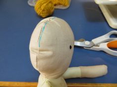 a stuffed doll sitting on top of a blue table next to scissors and yarns