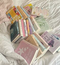 a pile of books sitting on top of a bed next to a white comforter